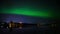 A 4k HD time-lapse of northern light dancing over a half-frozen lake and cloudy city light