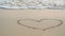 4K. heart drawing on sand beach with soft wave of the blue sea, ripple ocean wave with white bubble foam