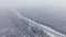 4K. Road in the winter forest with driving cars at snowfall. Aerial panoramic view.