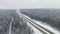 4K. Road in the winter forest with driving cars at snowfall. Aerial panoramic view. Vanishing perspective