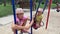 4k Sad twin sisters swinging on a swing on a playground.