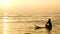 4K. silhouette of surfer man relax by sitting on surfboard over the sea at sunset on tropical beach. sport and recreation