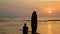 4K. silhouette of surfer man sitting on the sea beach with long surf boards at sunset on tropical beach