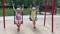 4k Smiling twins sisters swinging on a swing on a playground.