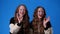 4k video of twin girls showing OK sign on blue background.