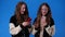 4k video of twin girls using their phones on blue background.