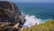 4K view of rugged cliffs at Praia Grande beach, Portugal. Atlantic White ocean waves hitting the rocky stone cliffs