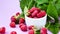 4k zoom in out Ripe red raspberries in white bowl with green leaves on background. Summer harvest fruits berries