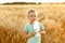 A 5-6-year-old boy stands in the middle of a field with a glass bottle of milk. A village child among the rye