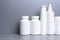 5 white jars for medicines and vitamins and dietary supplements without a name are on a gray shelf