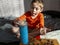 5-year-old boy puts 50 euro cent coin in savings jar,sit on bed,wooden box with scattered coins columns in front of him