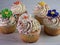 5 yellow cupcakes with white frosting and fondant flowers lined up on a limestone surface.  Festive and delicious to celebrate a