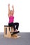 A 50-year-old trainer practices Pilates on an elevator chair, raising her arms high above her head. Seated