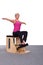 A 50-year-old trainer practices Pilates on an elevator chair, raising her arms to shoulder height and straightening to
