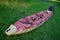 55-60 year old man lays out an inflatable kayak on the bright green grass. The boat is narrow and long. Clear sunny day, outdoors