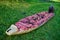 55-60 year old man lays out an inflatable kayak on the bright green grass. The boat is narrow and long. Clear sunny day, outdoors