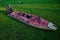 55-60 year old man lays out an inflatable kayak on the bright green grass. The boat is narrow and long. Clear sunny day, outdoors