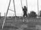 A 6-7 year old girl swinging on a swing against the background of a football field. Black and white monochrome image in retro