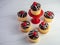6, half dozen, yellow cupcakes with chocolate frosting and a white drizzle with a a red cherry on top and, sitting on a sandstone