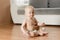 6 month infant sitting on a wooden floor wearing only a diaper