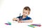 A 6 year old boy in a blue shirt paints with pencils on a white background isolate