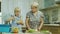 A 6-year-old girl in pink glasses prepares a salad in the kitchen. Her grandmother helps, use a tablet