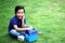 6 year old latino boy sitting on the grass with lunch box and colors for back to school