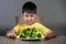 7 or 8 years old upset and disgusted Asian kid sitting on table in front of broccoli plate looking unhappy rejecting the fresh