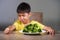 7 or 8 years old upset and disgusted Asian kid sitting on table in front of broccoli plate looking unhappy rejecting the fresh