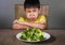 7 or 8 years old upset and disgusted hispanic kid sitting on table in front of broccoli plate looking unhappy rejecting the fresh