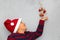 7 year old Latino boy with sweater and Christmas hat, holding Christmas tree with red spheres on gray background