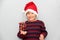 7 year old Latino boy with sweater and Christmas hat, holding Christmas tree with red spheres on gray background