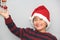 7 year old Latino boy with sweater and Christmas hat, holding Christmas tree with red spheres on gray background