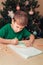 7 years old boy write letter to Santa sitting by desk