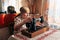 70 years old woman sewing at home, senior seamstress sitting at desk in front of sewing machine, her hands pushing pink fabric