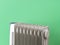 9 fins oil filled electric heater against green background. Portable domestic appliance for heating home in a cold season. Gray
