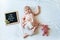 9 Nine months old baby girl laying down on white background with letter board and teddy bear. Flat lay composition.