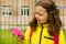 A 9-year-old blonde girl in a yellow jacket with a pink briefcase stands near the school and holds a pink mask in her hand.