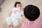 A 9-year-old boy is playing in bed with his 3-month-old newborn sister. An Asian boy is taking care of his sister in bed while