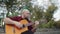 Aalternative man sitting on the walkway at park and playing guitar