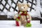 Abandoned beige plushy teddy bear with red green striped knitted scarf sitting on the bench covered with white snow