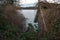 Abandoned boat house, rotting wooden dock and an old boat overgrown with brambles and wild clematis on the shore of a lake at a