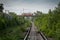 Abandoned empty unused railway track in the forest with a red tram in the background, traveling over the overpass