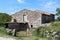 Abandoned family house built in traditional stone style with wooden window blinds and wooden doors surrounded with uncut grass and