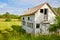 Abandoned farm house in grassy field near farmland with busted windows and door