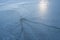 Abandoned fishing hole with frozen long ice cracks on empty river surface with footprints, mysterious sun backlight