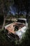 Abandoned French car under pine trees, with an old house in the background