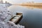 Abandoned little boat moored by the river bank in winter. Calm river, morning, sun and frost