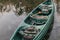 Abandoned old green plastic canoe with paddle beside the lake background.