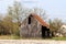 Abandoned old wooden barn with broken dilapidated wooden boards next to unused paved parking lot surrounded with uncut grass